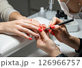 A close-up view of a manicurist expertly applying vibrant red nail polish to a client's fingernails, illustrating the pampering and beauty ritual of a professional manicure 126966757