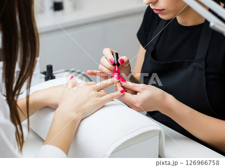 A close-up view of a manicurist expertly applying vibrant red nail polish to a client's fingernails, illustrating the pampering and beauty ritual of a professional manicure 126966758