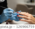A close-up view of a manicurist expertly applying vibrant red nail polish to a client's fingernails, illustrating the pampering and beauty ritual of a professional manicure 126966759