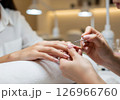 A close-up view of a manicurist expertly applying vibrant red nail polish to a client's fingernails, illustrating the pampering and beauty ritual of a professional manicure 126966760