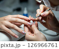 A close-up view of a manicurist expertly applying vibrant red nail polish to a client's fingernails, illustrating the pampering and beauty ritual of a professional manicure 126966761