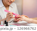 A close-up view of a manicurist expertly applying vibrant red nail polish to a client's fingernails, illustrating the pampering and beauty ritual of a professional manicure 126966762