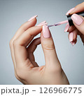 Close-up of a woman's hands meticulously applying vibrant red nail polish, showcasing the beauty and precision of a fresh manicure 126966775