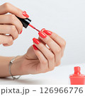 Close-up of a woman's hands meticulously applying vibrant red nail polish, showcasing the beauty and precision of a fresh manicure 126966776