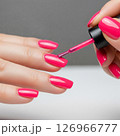 Close-up of a woman's hands meticulously applying vibrant red nail polish, showcasing the beauty and precision of a fresh manicure 126966777