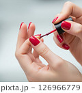 Close-up of a woman's hands meticulously applying vibrant red nail polish, showcasing the beauty and precision of a fresh manicure 126966779