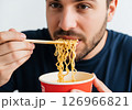 Close-up of a person slurping hot, steamy noodles directly from a bowl, showcasing the enjoyment of a quick and delicious meal. 126966821