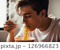 Close-up of a person slurping hot, steamy noodles directly from a bowl, showcasing the enjoyment of a quick and delicious meal. 126966823