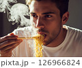 Close-up of a person slurping hot, steamy noodles directly from a bowl, showcasing the enjoyment of a quick and delicious meal. 126966824