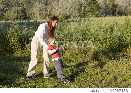 Mother and son enjoying a sunny day in the field, playing with wild plants 126967178