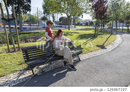Mother and son sharing a snack on park bench on a sunny day Mother and son sharing a snack on park bench on a sunny day 126967197