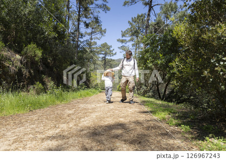 Father and son hiking together on sunny forest trail Father and son hiking together on sunny forest trail 126967243