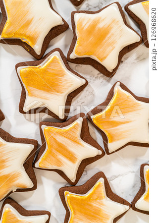 A collection of gingerbread star cookies decorated with royal icing and painted with vibrant gold luster dust, beautifully arranged for a festive look. 126968620