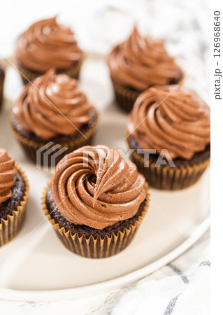 Freshly baked cupcakes have been masterfully infused with rich caramel and adorned with velvety chocolate frosting, all elegantly presented on a pristine white serving plate. Freshly baked cupcakes have been masterfully infused with rich caramel and adorned with velvety chocolate frosting, all elegantly presented on a pristine white serving plate. 126968640