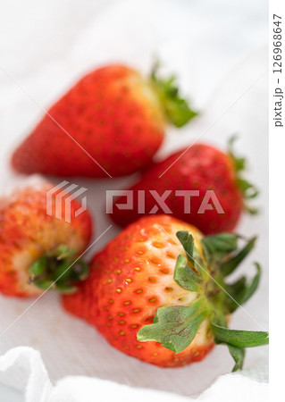 Bright red strawberries, interspersed with signs of mold, rest in a glass bowl lined with a paper towel on a white napkin, indicating improper storage techniques. Bright red strawberries, interspersed with signs of mold, rest in a glass bowl lined with a paper towel on a white napkin, indicating improper storage techniques. 126968647
