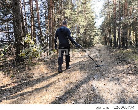 A man treasure hunter with a metal detector in the forest. Treasure hunter on a mission exploring the forest with a metal detector in search of lost history and hidden gems. 126969774