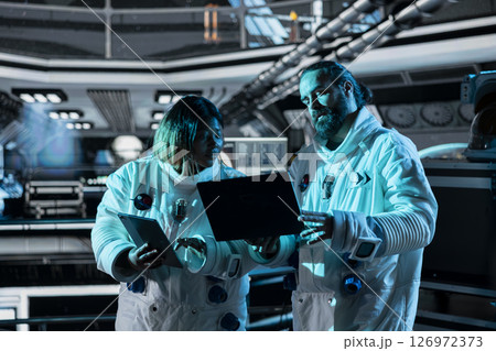 Teamworking astronauts doing brainstorming to confirm suit integrity using laptop. Orbital station colleagues talking, testing gear during routine equipment check using notebook Teamworking astronauts doing brainstorming to confirm suit integrity using laptop. Orbital station colleagues talking, testing gear during routine equipment check using notebook 126972373