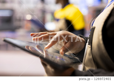 Smart factory engineer using a tablet to develop production line layouts in CAD software. Close up of african american worker optimizing industrial floor configurations with digital tool. Smart factory engineer using a tablet to develop production line layouts in CAD software. Close up of african american worker optimizing industrial floor configurations with digital tool. 126972401