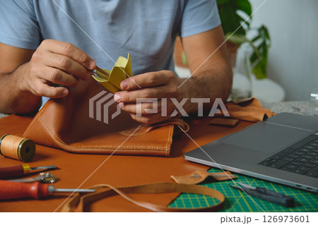 Leather craftsman gluing lining to brown leather bag in workshop Leather craftsman gluing lining to brown leather bag in workshop 126973601