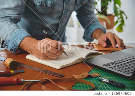 Leather craftsman drawing a new design on notebook in his workshop 126973609