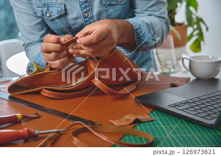 Leather craftsman sewing a bag in workshop 126973621