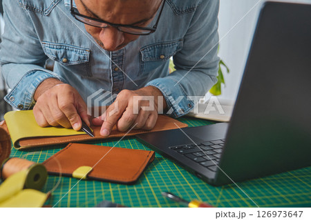 Craftsman working leather at desk with laptop and tools Craftsman working leather at desk with laptop and tools 126973647