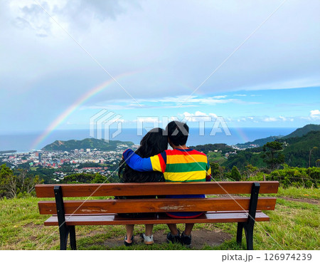 AI generated loving LGBTQ couple lady boy in feminine attire and a man in a rainbow shirt embracing on field with a rainbow sky. Represents diversity, acceptance, and romantic love. 126974239