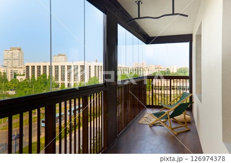 spacious and bright balcony with upholstered chairs, stylish and modern glazing, clear sunny weather 126974378