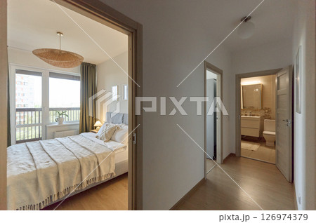 Cozy bedroom interior, beige bedspread and pillow, bedside lamp next to the bed, light from the window 126974379