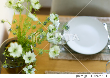 a bouquet of daisies in a glass vase stands on a table on a white background, a wine glass, table setting, plates, defocus, macrophotography, bokeh 126974391