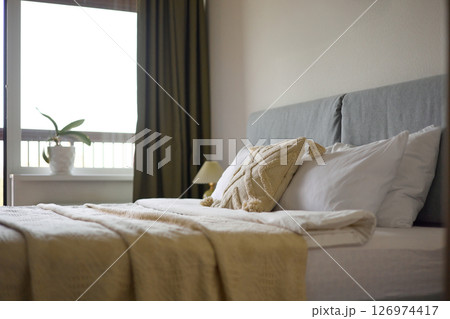 Cozy bedroom interior, beige bedspread and pillow, bedside lamp next to the bed, light from the window Cozy bedroom interior, beige bedspread and pillow, bedside lamp next to the bed, light from the window 126974417