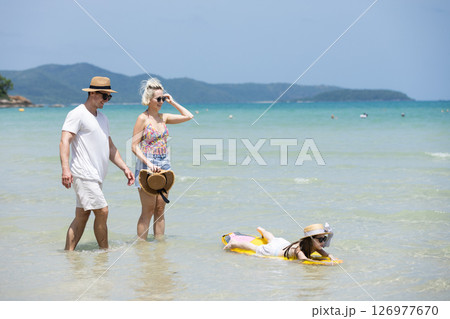 Happy family relax walking on beach with daughter on surfboard. Joyful vacation with parents and children at the sea Trip enjoying bonding. together. 126977670