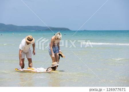Happy family relax walking on beach with daughter on surfboard. Joyful vacation with parents and children at the sea Trip enjoying bonding. together. 126977671