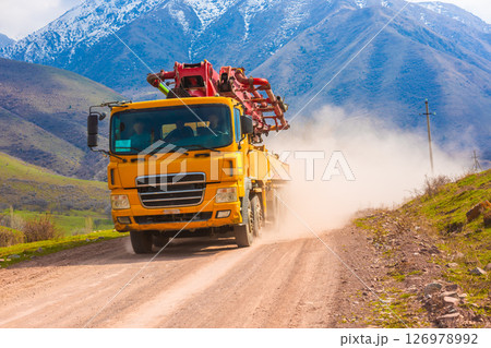 Front view of a yellow concrete pump truck on a dusty mountain road. 126978992