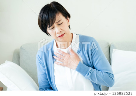 ソファで胸に手を当てる中高年女性 ソファで胸に手を当てる中高年女性 126982525