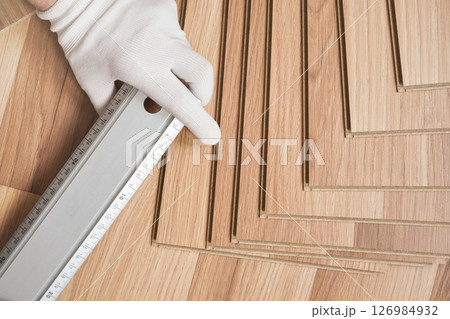 Installing laminated floor, detail on hand in white gloves holding steel ruler over wooden tiles Installing laminated floor, detail on hand in white gloves holding steel ruler over wooden tiles 126984932