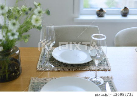 a bouquet of daisies in a glass vase stands on a table on a white background, a wine glass, table setting, plates, defocus, macrophotography, bokeh 126985733