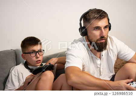 Father and son playing video games together on a couch, enjoying quality time. 126986510