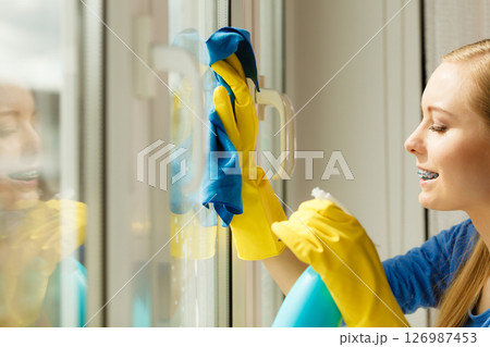 Girl cleaning window at home using detergent rag 126987453