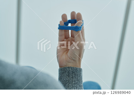 man exercises his fingers with a blue elastic band 126989040