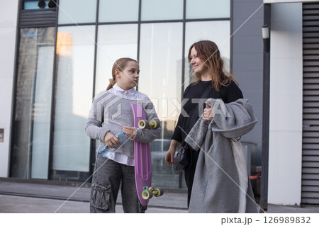 Portrait of mom and kid girl with skateboard in her hands outdoors Portrait of mom and kid girl with skateboard in her hands outdoors 126989832
