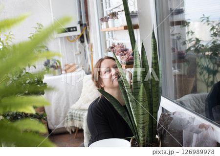 Pretty mid adult woman holding green houseplant in her hand standing indoor. Pretty mid adult woman holding green houseplant in her hand standing indoor. 126989978