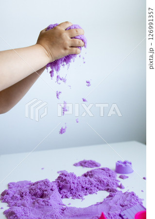 Child playing with purple kinetic sand on white table 126991357