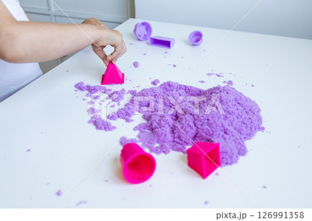 Child hand playing with purple sand and molds on white table 126991358