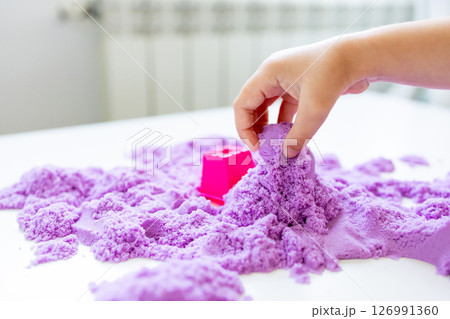 Child hand playing with purple kinetic sand and pink mold on table 126991360