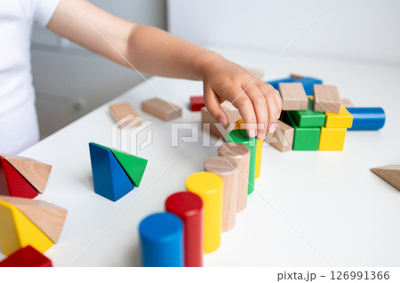 Child playing with colorful geometric blocks on white table 126991366