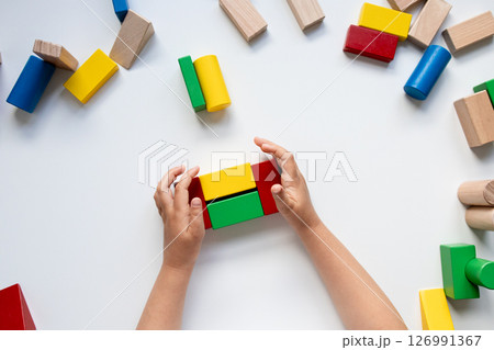 Child hands building with colorful wooden blocks on a white surface Child hands building with colorful wooden blocks on a white surface 126991367