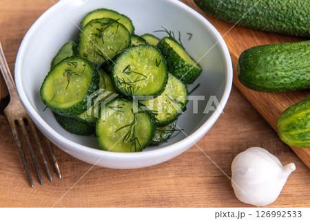 Organic cucumbers slices in a ceramic white bowl on a wooden table. Organic cucumbers slices in a ceramic white bowl on a wooden table. 126992533