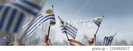 Uruguay flags in their hands on a blurred urban background Uruguay flags in their hands on a blurred urban background 126992657