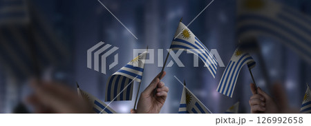Uruguay flags in their hands on a blurred urban background 126992658